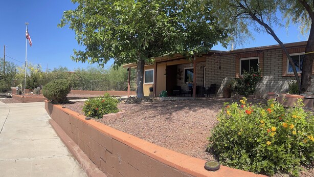 A brick building with a patio area, a flag, and various plants. - Quiet spacious home in Cul-de-sac near downtown (Tucson)