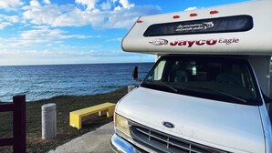 A white Jayco Eagle RV parked by the ocean with a clear sky. - Travel PR! (San Juan)
