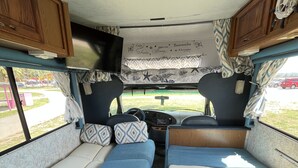 A compact RV interior with two sleeping areas, a central table, and a steering wheel. - Travel PR! (San Juan)