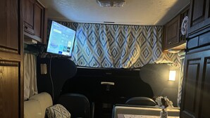 A compact RV interior with a kitchenette, a seating area with two couches, and a small table with a vase. - Travel PR! (San Juan)