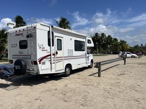Un camping-car Jayco Eagle blanc est garé sur une plage de sable, avec des palmiers en arrière-plan.