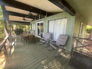 Eine überdachte Terrasse im Freien mit Tisch und Stühlen, einem Deckenventilator und Blick auf den umliegenden Wald.