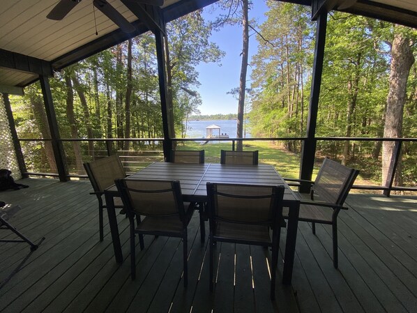 Eine überdachte Terrasse mit Tisch und Stühlen mit Blick auf einen See und einen bewaldeten Bereich.