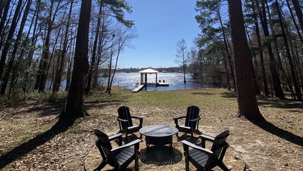 A gazebo overlooking a lake, surrounded by tall trees and two Adirondack chairs facing the water. - Shore Thing Waterfront Home with private covered boat dock on Toledo Bend (Hemphill)