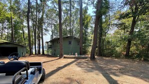 A rustic cabin with a dirt driveway, surrounded by tall trees. - Shore Thing Waterfront Home with private covered boat dock on Toledo Bend (Hemphill)