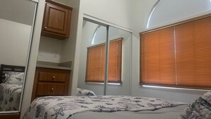 Een slaapkamer met een bed, een kledingkast, een spiegel en een raam met zonwering.