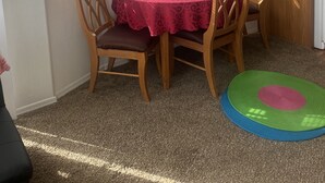 Een eethoek met een tafel bedekt met een rode tafelkleed, twee houten stoelen en een wandklok.