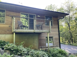 Een houten chalet met twee verdiepingen en een balkon, omringd door weelderige begroeiing.