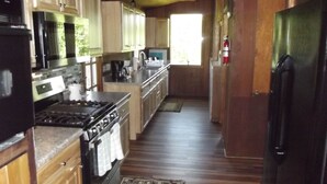 Une cuisine avec des meubles de rangement en bois, une cuisinière, un réfrigérateur et une fenêtre qui laisse entrer la lumière naturelle.