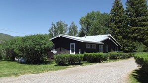 Une cabane en rondins avec une allée en gravier et une végétation luxuriante tout autour.