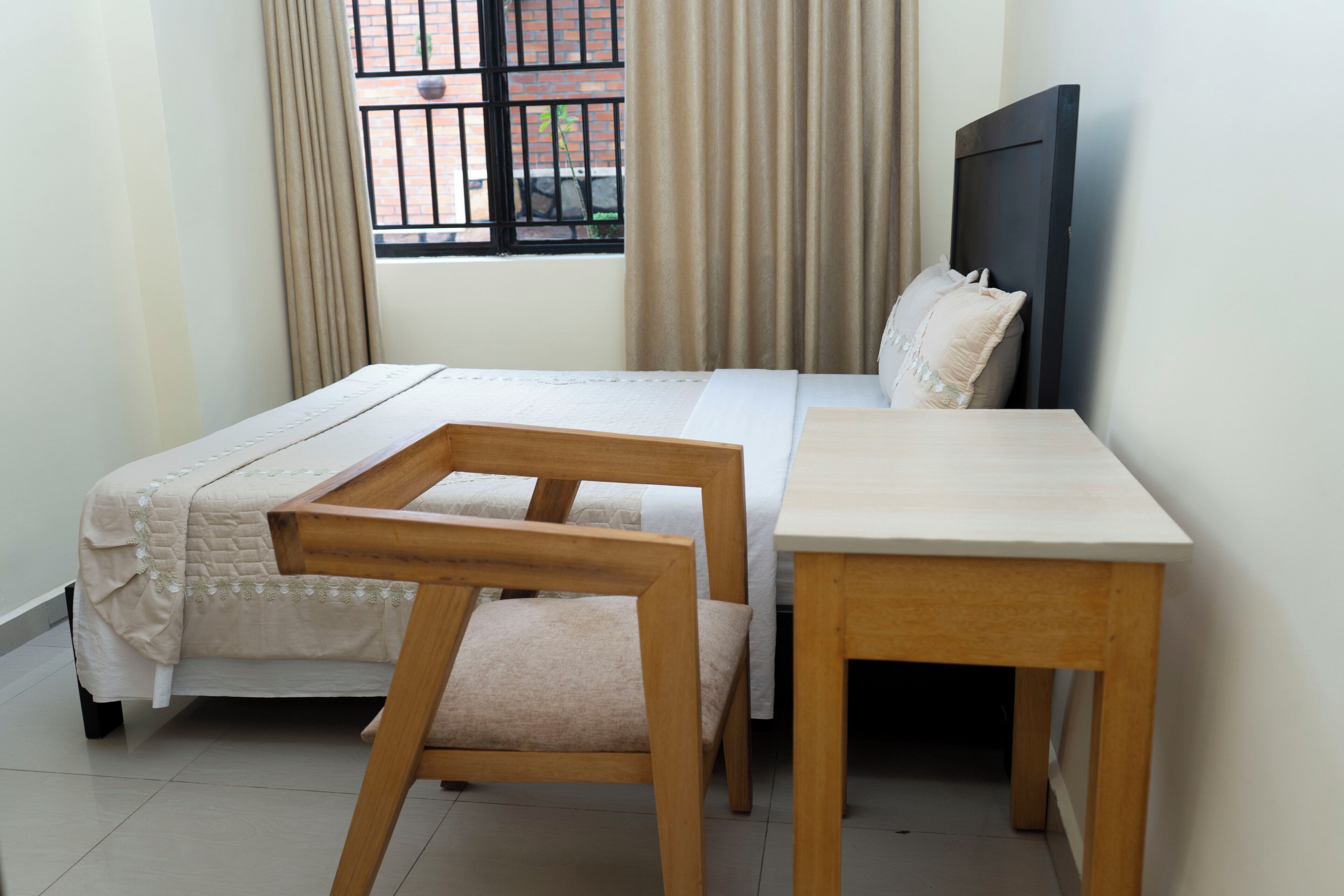Una camera da letto ordinata con un letto, una sedia di legno, un tavolino e una finestra con tende.
