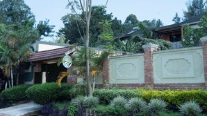 A residential house with a brick exterior, a covered porch, and lush greenery including palm trees and various shrubs.