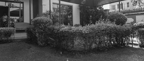A modern building with a covered outdoor area, surrounded by well-maintained bushes and a lawn.