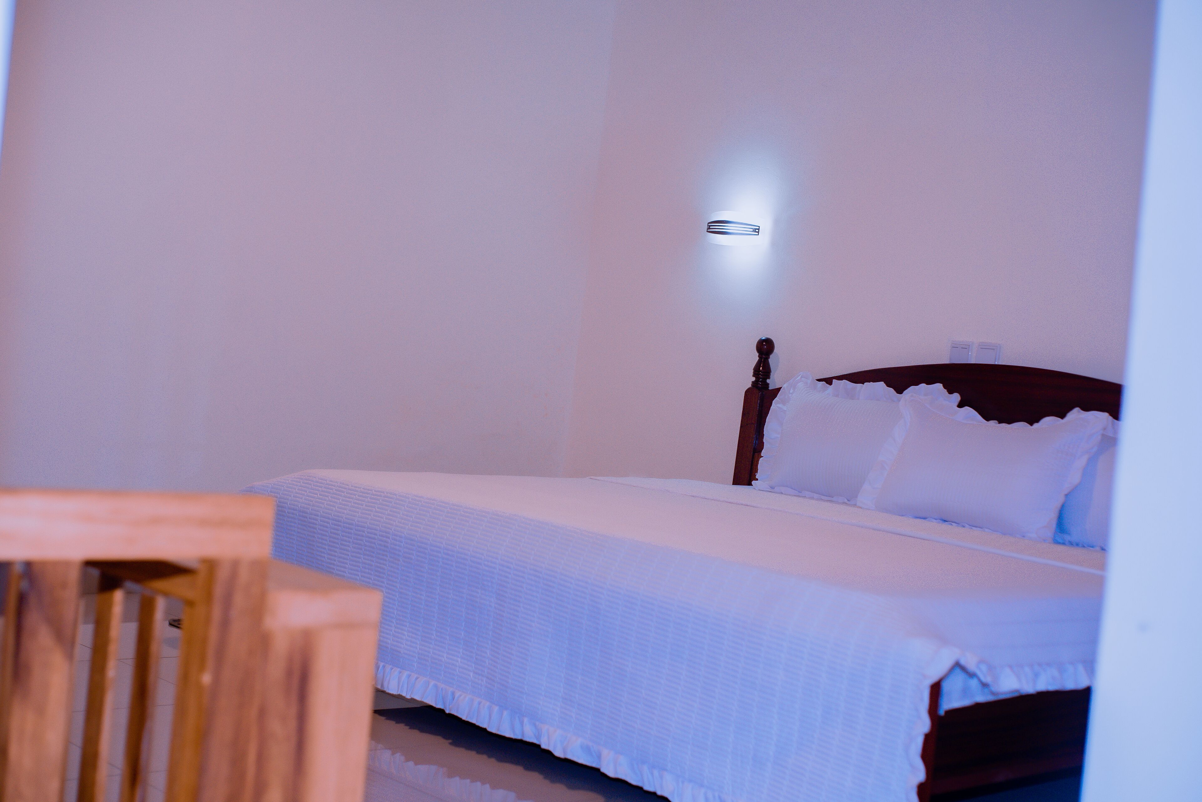 A bedroom with a single bed, a nightstand, and a wall-mounted light.