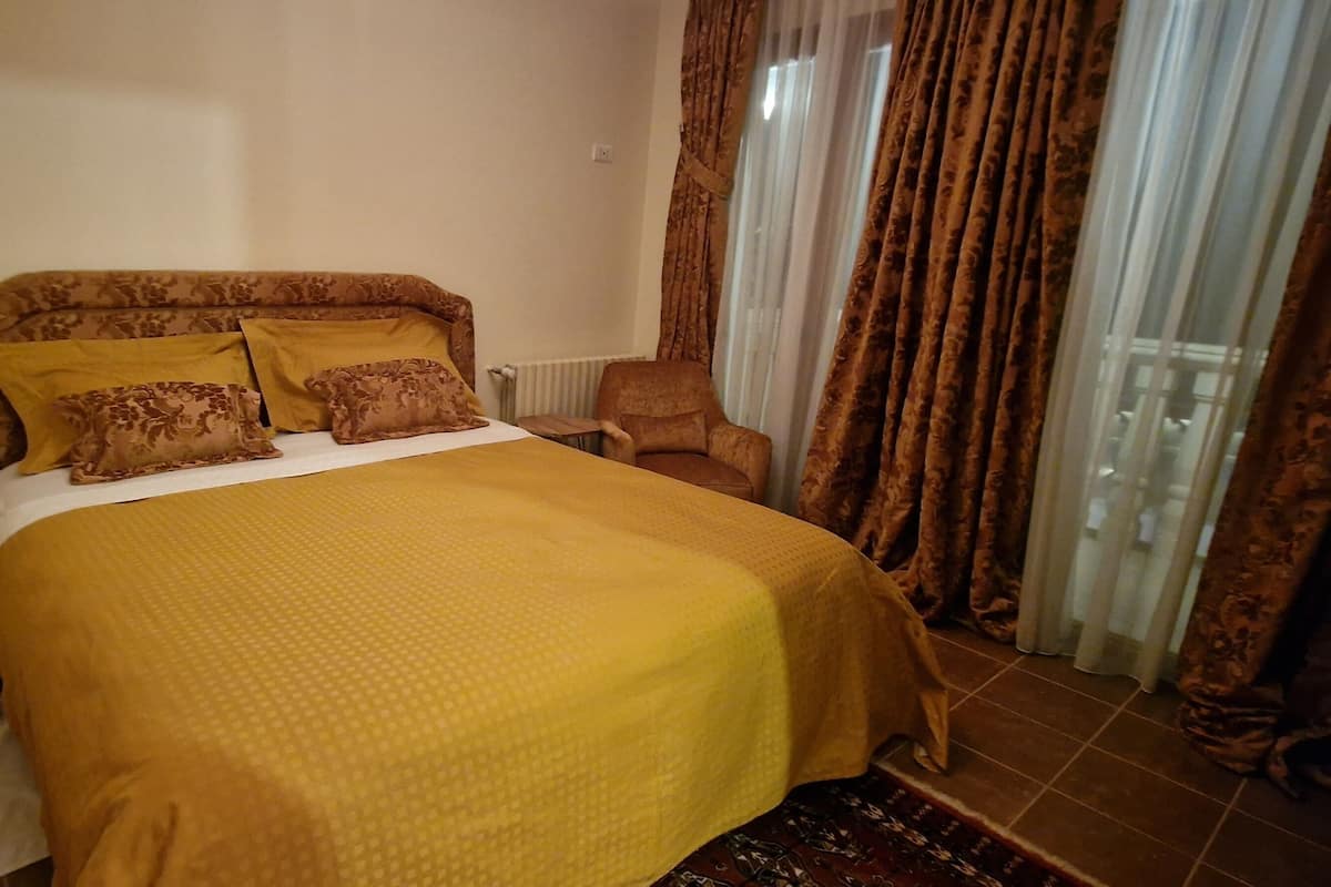 Una habitación de hotel con cama, una silla, una mesita de noche y una ventana con cortinas.