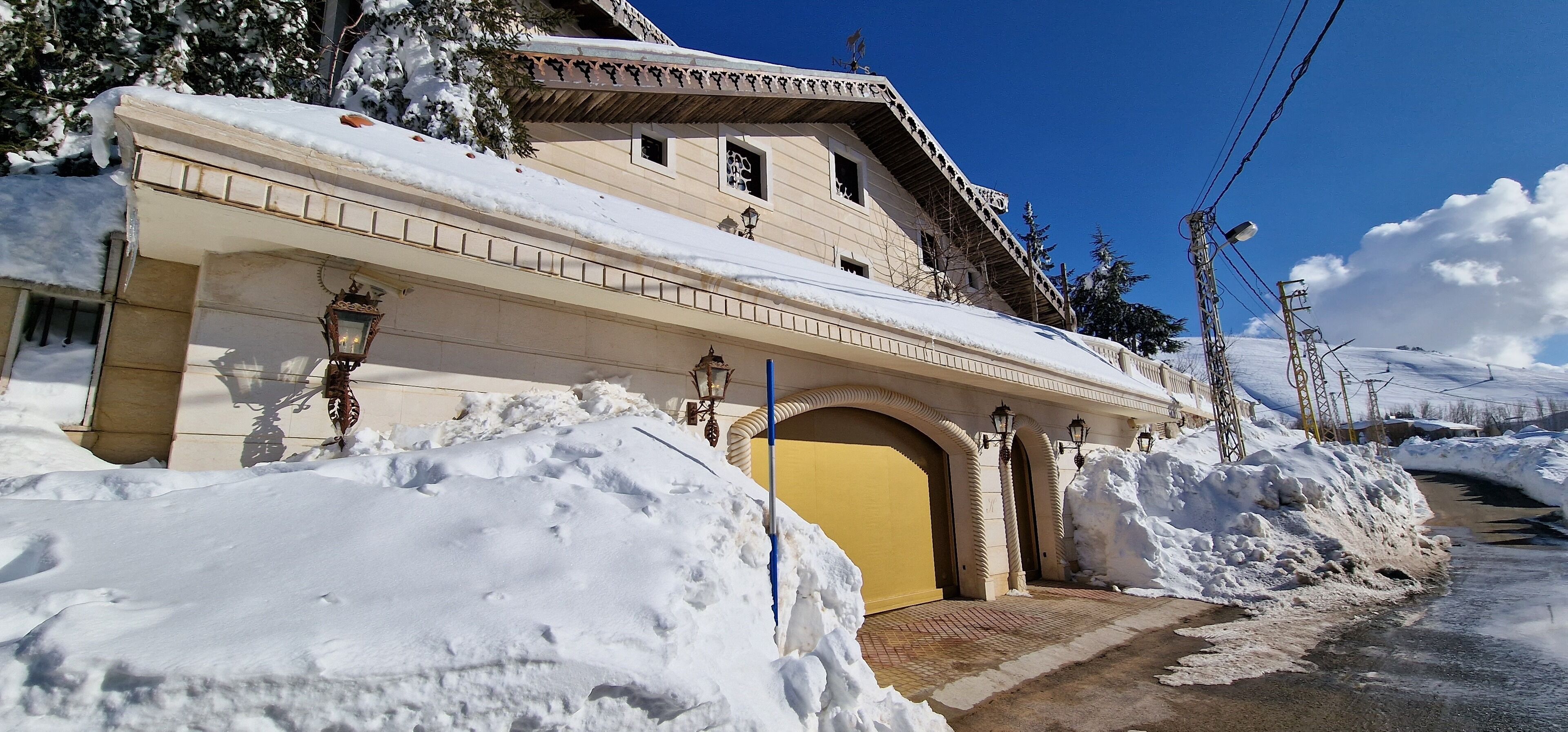 Un edificio cubierto de nieve con una entrada amarilla, un vestíbulo cubierto y un paisaje nevado.