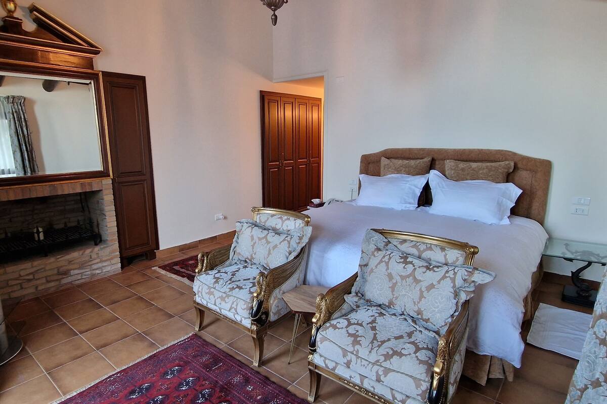 Un dormitorio con cama, dos sillones, televisor y chimenea.