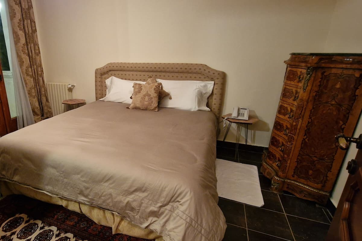 Habitación de hotel con una cama grande, un armario de madera, una mesita pequeña y una silla.