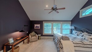Ein Schlafzimmer mit Bett, Deckenventilator, Fenster mit Jalousien, Nachttisch und Beistelltisch.