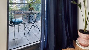 En balkon med udsigt til høje bygninger, et bord med en stol og en potteplante.