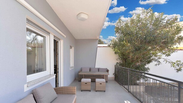 Ein Balkon mit einer Couch, zwei Hocker, einem Tisch und einem Geländer.