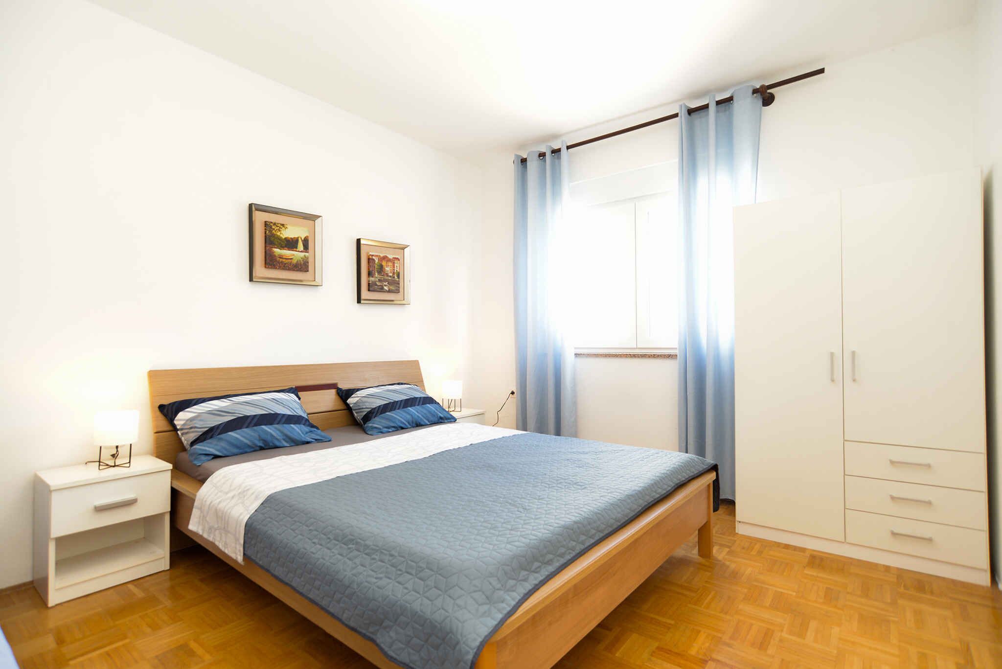 A bedroom with a wooden bed, a nightstand, a wardrobe, and two framed pictures on the wall.
