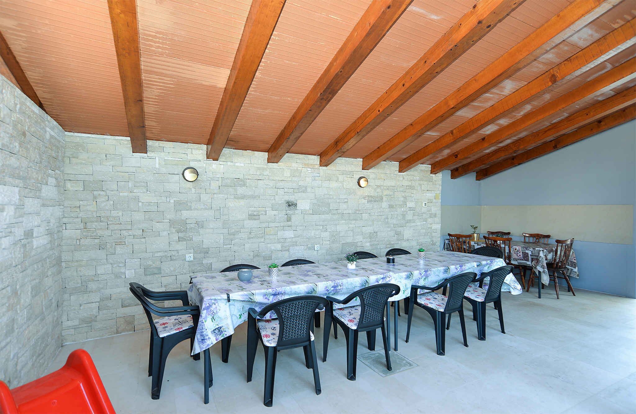 A covered outdoor dining area with stone walls, wooden beams, and a tiled floor.