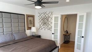 A bedroom with a tufted headboard, a bed with a brown quilt, a bedside lamp, a wall-mounted abstract art piece, and a door leading to another room. - Cozy penthouse Atlanta (Atlanta)