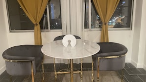 A dining area with a round table and two chairs, a window with curtains, and a city view at night. - Cozy penthouse Atlanta (Atlanta)