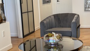 A modern living room with a grey armchair, a glass coffee table with decorative items, and a wooden floor. - Cozy penthouse Atlanta (Atlanta)