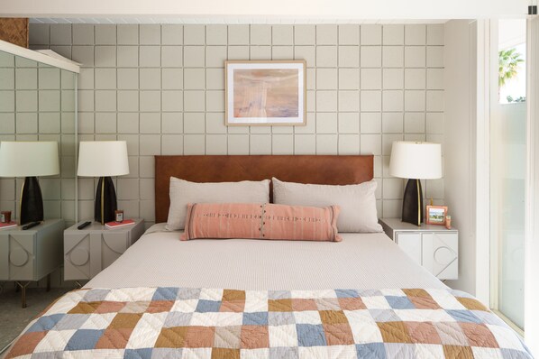 A neatly made bed with a checkered quilt, two bedside lamps, and a framed picture on the wall.