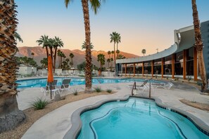 A pool area with lounge chairs, palm trees, and a modern building with large windows.