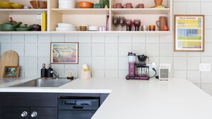 A kitchen with white cabinets, a coffee maker, and a framed picture on the wall. - New to VRBO! MidCentury Modern Bungalow @ Ocotillo Lodge (Palm Springs)