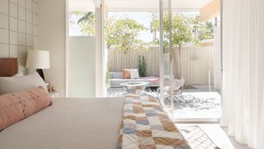 A bedroom with a large bed, a nightstand, a lamp, and a view of an outdoor patio with a sofa, chairs, and a table. - New to VRBO! MidCentury Modern Bungalow @ Ocotillo Lodge (Palm Springs)