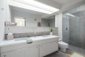 Une salle de bain moderne dotée d’un grand miroir, de deux lavabos, de toilettes et d’une douche à parois de verre.