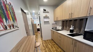 Une cuisine moderne avec des meubles en bois, un évier en acier inoxydable et un four à micro-ondes. On y trouve une table à manger en bois avec des tabourets, et un tableau abstrait aux couleurs vives accroché au mur.