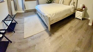 A bedroom with a bed, a nightstand, a chair, a window with curtains, a ceiling fan, and a plant.