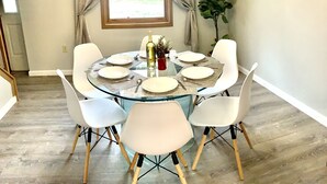 A round glass dining table with white chairs, a bottle of wine, and a small plant on the table.