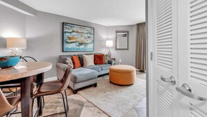 A modern living room with a round table, a sofa, an ottoman, and a painting on the wall. - Oceanfront Perfect Couples Getaway (Myrtle Beach)