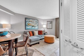 A modern living room with a round table, a sofa, an ottoman, and a painting on the wall. - Oceanfront Perfect Couples Getaway (Myrtle Beach)