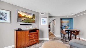 A modern living room with a wooden cabinet, a flat-screen TV, and a dining area with a table and chairs. - Oceanfront Perfect Couples Getaway (Myrtle Beach)