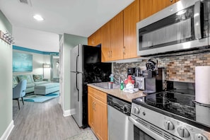 A compact kitchen with wooden cabinets, a stainless steel refrigerator, a microwave, a coffee maker, and a dishwasher.