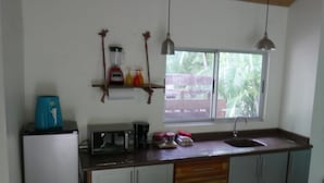 Une cuisine équipée d’un évier, de placards, d’une machine à café et d’une fenêtre donnant sur un espace verdoyant.