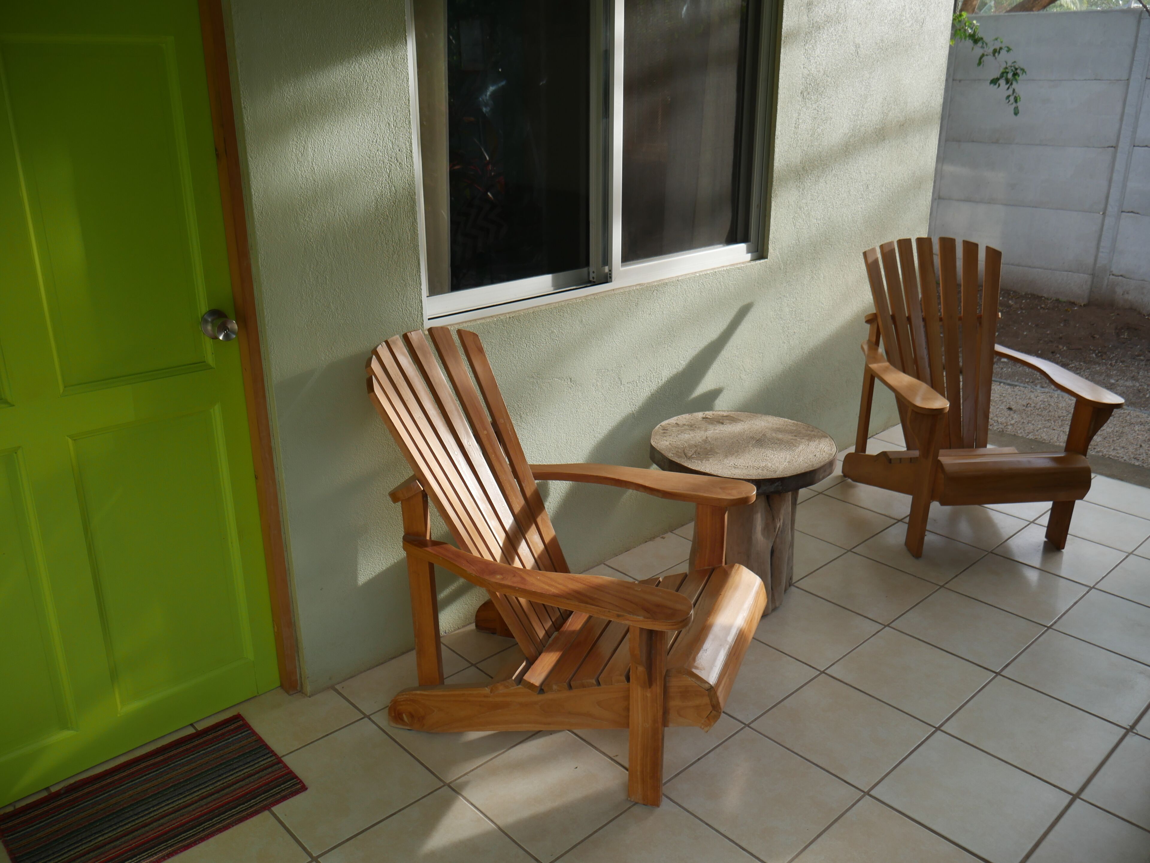 Two wooden chairs and a small round table in a room with a green door and a window.