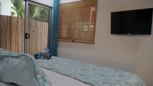 Une chambre à coucher avec un lit, un téléviseur fixé au mur et une fenêtre avec des stores.