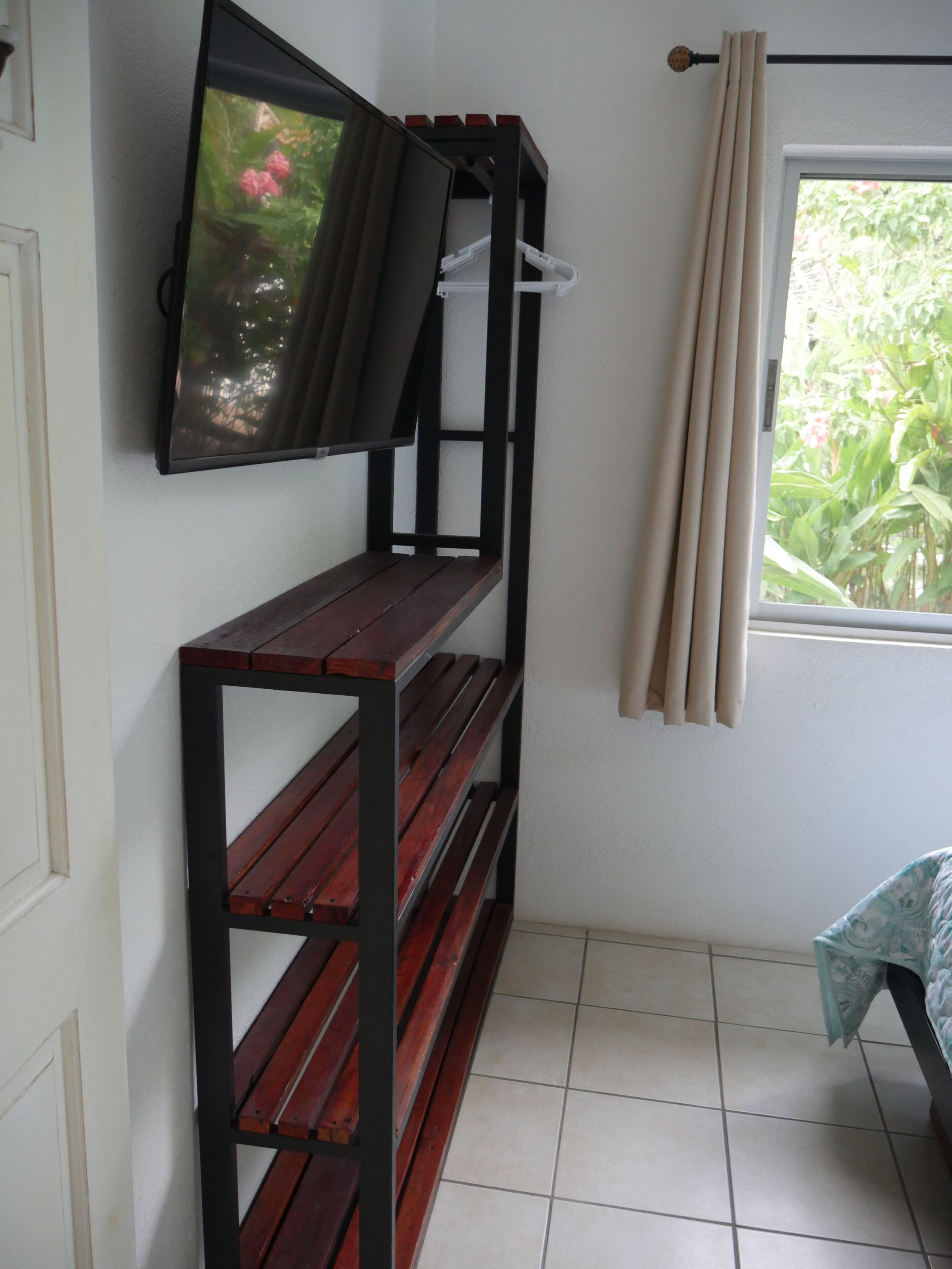 Une pièce avec un banc en bois, un téléviseur fixé au mur et une fenêtre avec des rideaux.