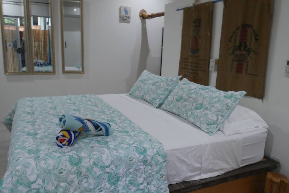 A bed with a patterned bedspread and pillows, a wooden headboard, and a small wooden stool.