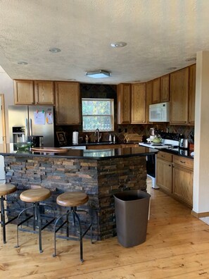 A kitchen with wooden cabinets, a stone island, and a stainless steel refrigerator. - Breathtaking Breckenridge Mountain Escape (Breckenridge)