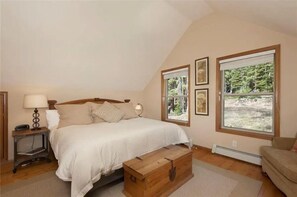 A bedroom with a bed, bedside tables, a wooden chest, and large windows with a view of trees. - Breathtaking Breckenridge Mountain Escape (Breckenridge)