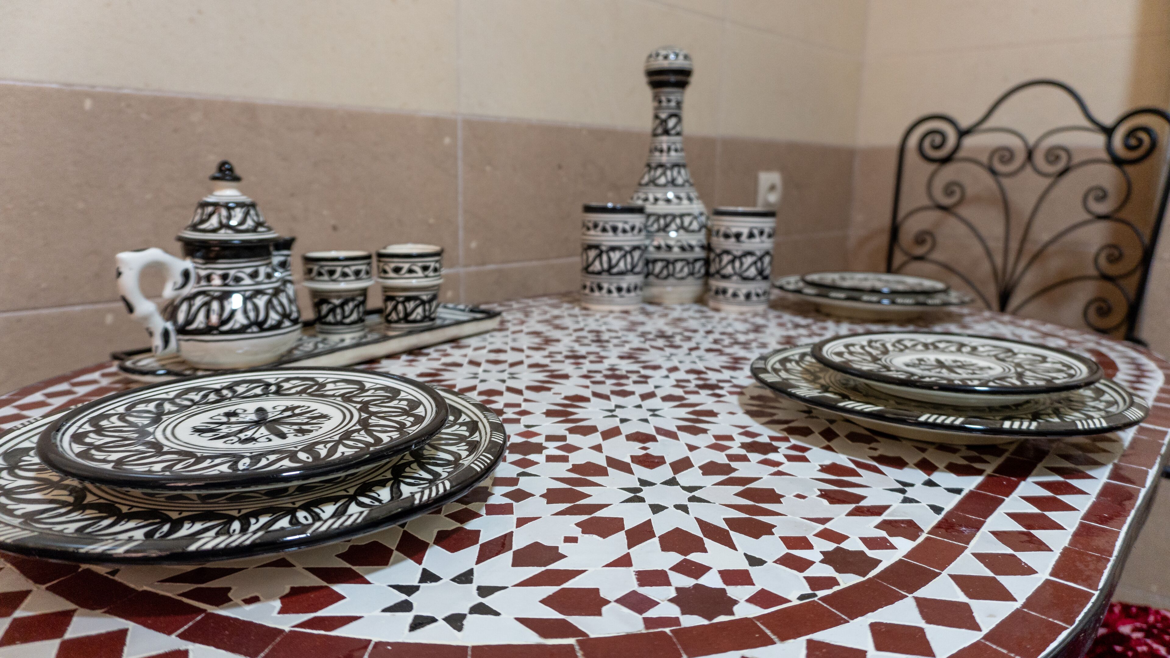 Une table ornée d’un motif de mosaïque, entourée d’une vaisselle aux motifs noir et blanc comprenant des assiettes, des tasses et une théière.